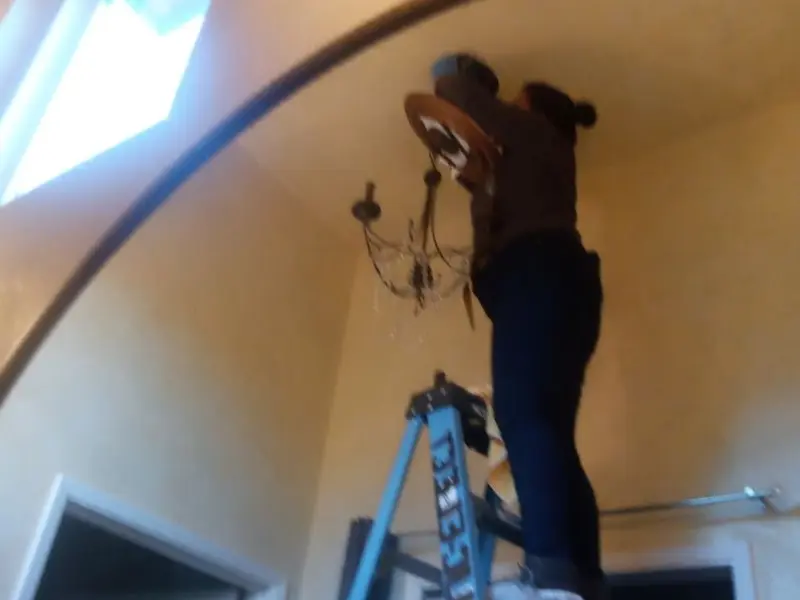 Electrician installing a chandelier in a Westwood residence